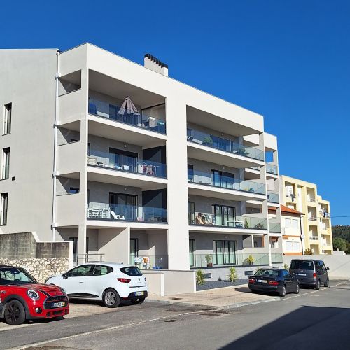 An exterior view of the apartment building with parking spaces and cars along the street.