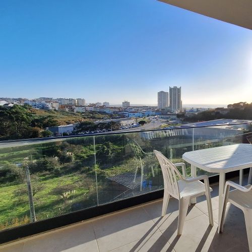 A terrace with white garden furniture and a view of two high-rise buildings and the sea