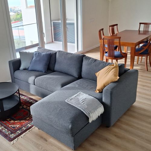 A living room with a gray sofa, a red rug, and a dining table in the background.