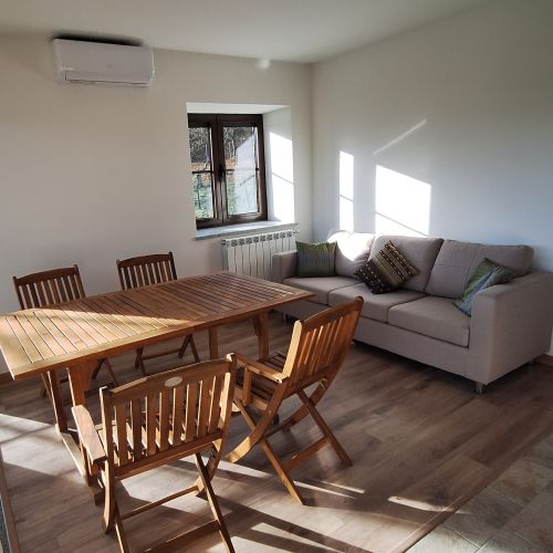 A living room with a brown wooden dining table and a gray sofa with green cushions